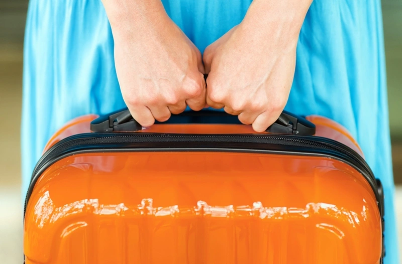 an orange suitcase held by a woman with a blue dress.