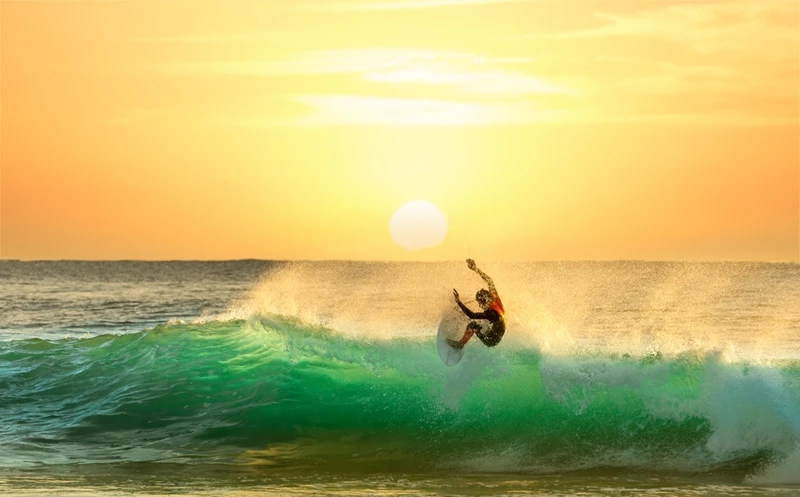 A lone surfer riding a wave at sunrise