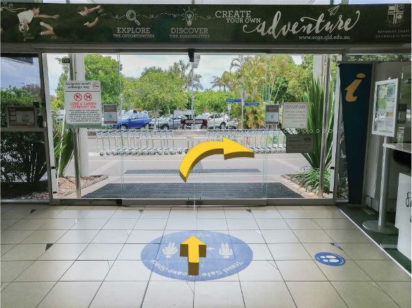 A glass door at the exit of the Sunshine Coast Airport with two yellow arrows. One pointing straight and the other pointing right outside of the building.