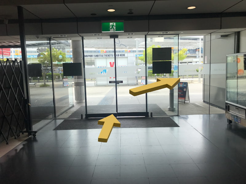 Glass doors inside airport terminal. Yellow arrows directing to exit the building and turn right