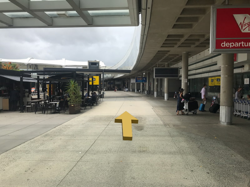 Sidewalk running beside Brisbane Airport. A red Virgin Departures sign on the right.