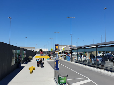 Sidewalk at airport with pedestrian shelters to the right and crosswalk in the distance.