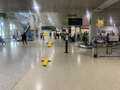 Airport terminal with baggage carousels on the right and escalators on the left.