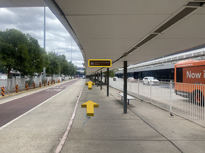 Sheltered walkway next to airport terminal and shuttle bus pickup area.