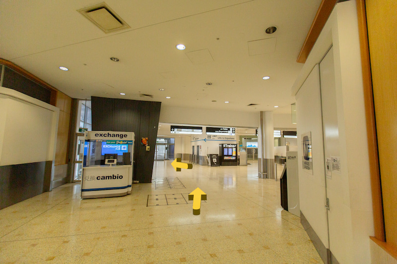 Hallway with white walls and currency exchange on the left - directional signs pointing to the right.