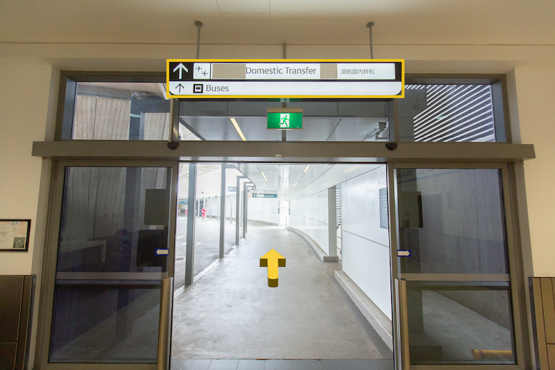 Glass doors open to outside with a directional sign above pointing to domestic transfer and buses.