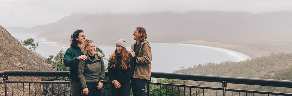 Four people laughing with overlooking the ocean's bay.