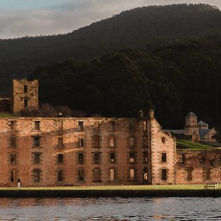 Historic Brick building surrounded by forest and water.