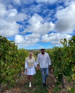 Couple wearing white walking through vineyards.