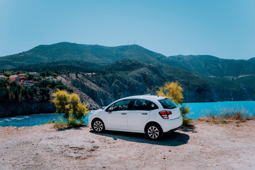 White car parked on a cliff that overlooks a lake | Featured image for the Tips for Choosing a Rental Car blog for East Coast Car Rentals.