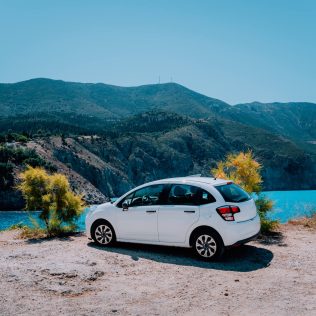 White car parked on a cliff that overlooks a lake | Featured image for the Tips for Choosing a Rental Car blog for East Coast Car Rentals.